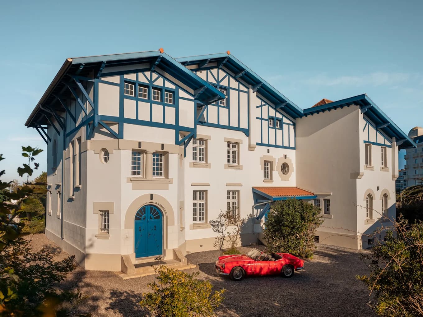 La façade de la Maison Resaurie : enduit blanc, colombages bleus, gravier devant le perron.